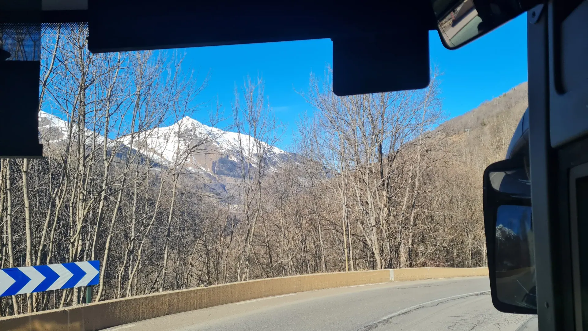 Snow-capped mountains and a winding road seen through a bus windscreen