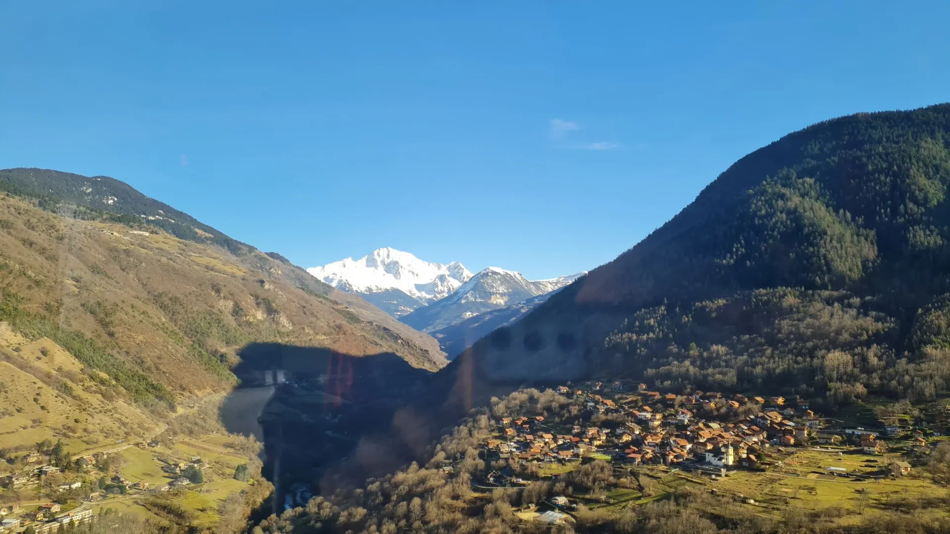 A mountain valley with a village and a snow-capped peak under a clear blue sky