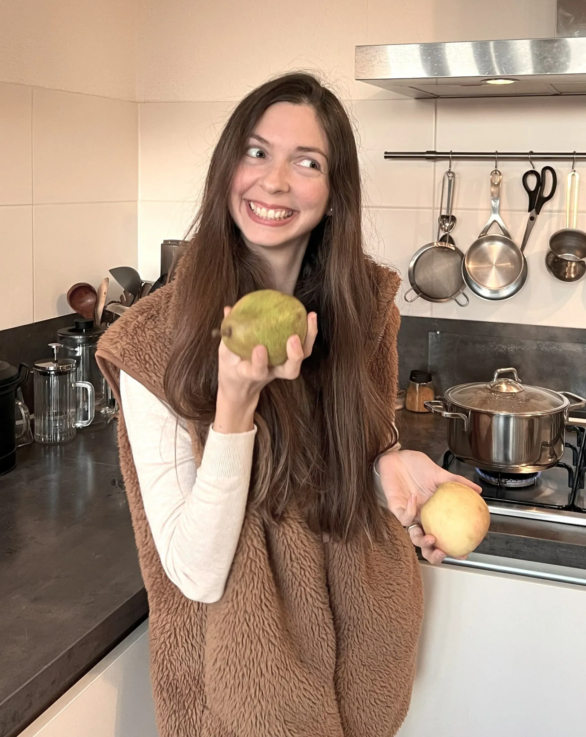 Ece smiling in a kitchen, holding a piece of fruit in each hand