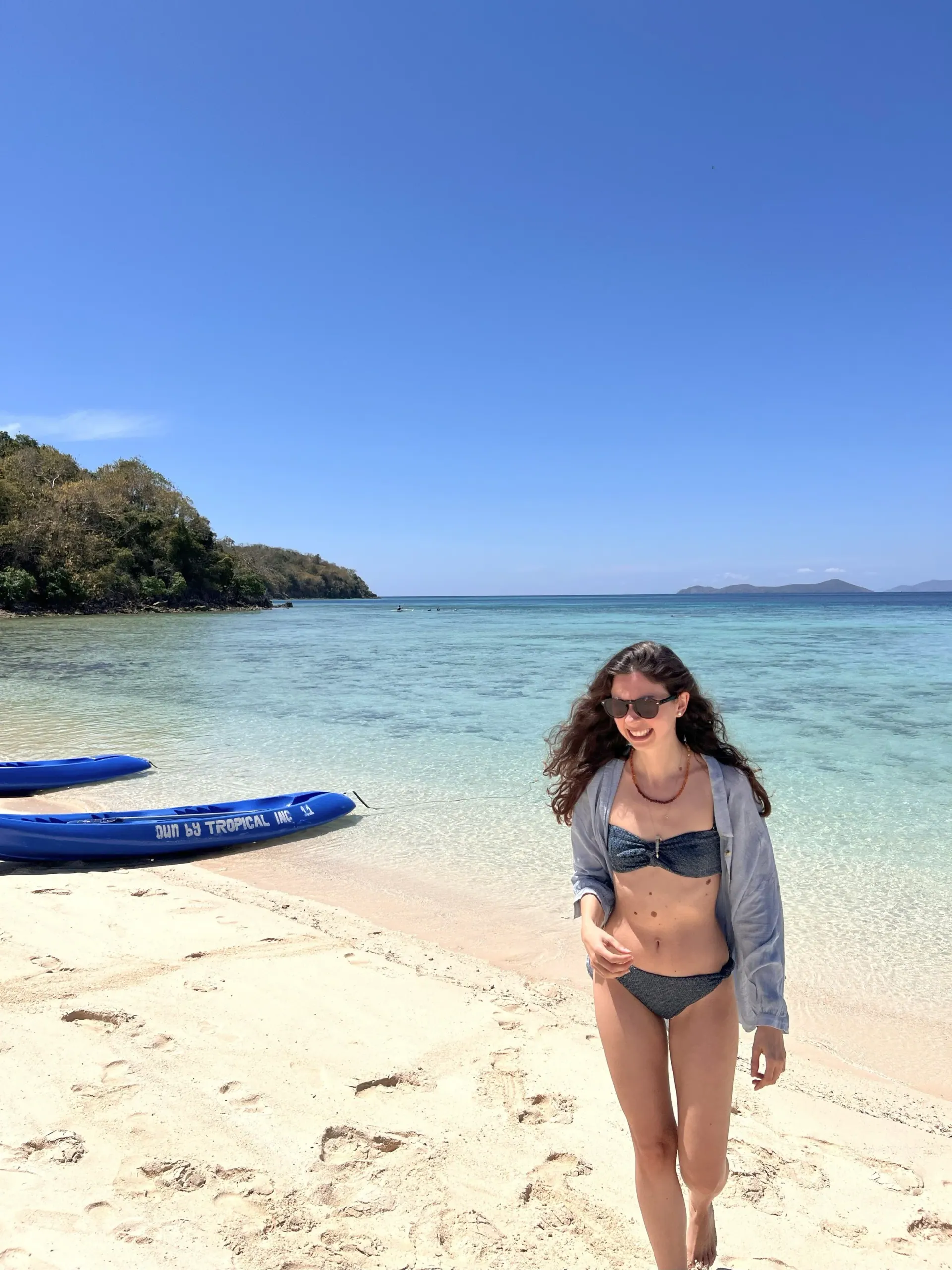 Ece walking on a white sand beach beside clear turquoise water