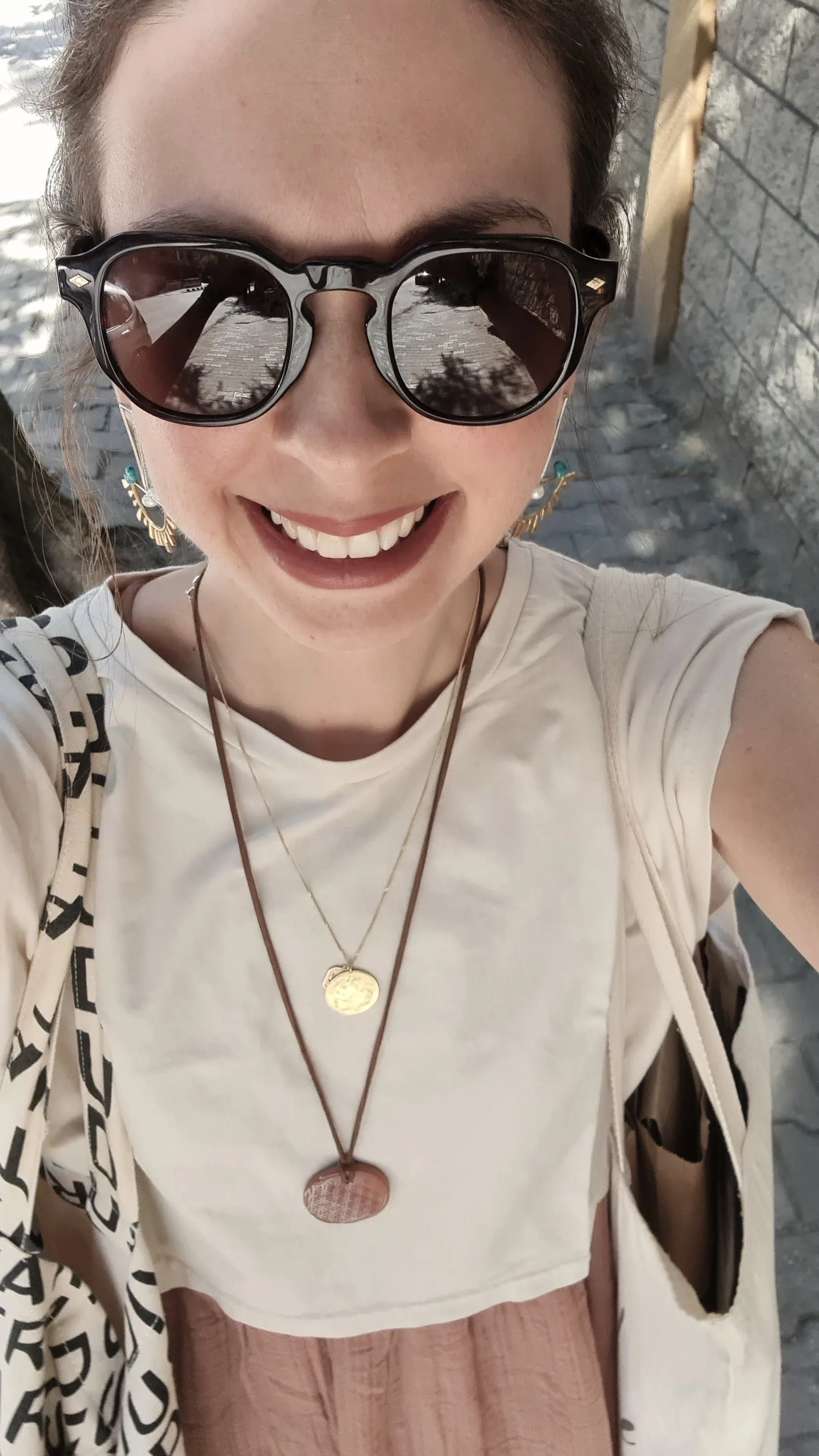 Smiling selfie of Ece in dark sunglasses, a cream top and layered necklaces