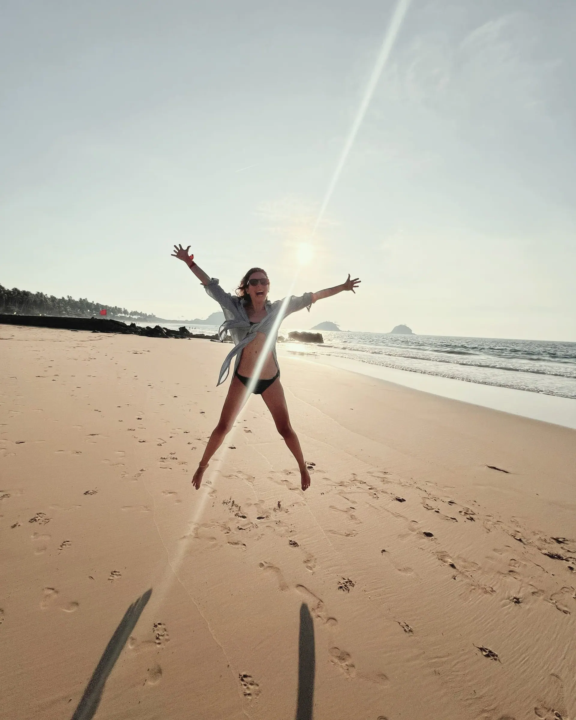 Ece jumping with her arms spread wide on a sunny beach