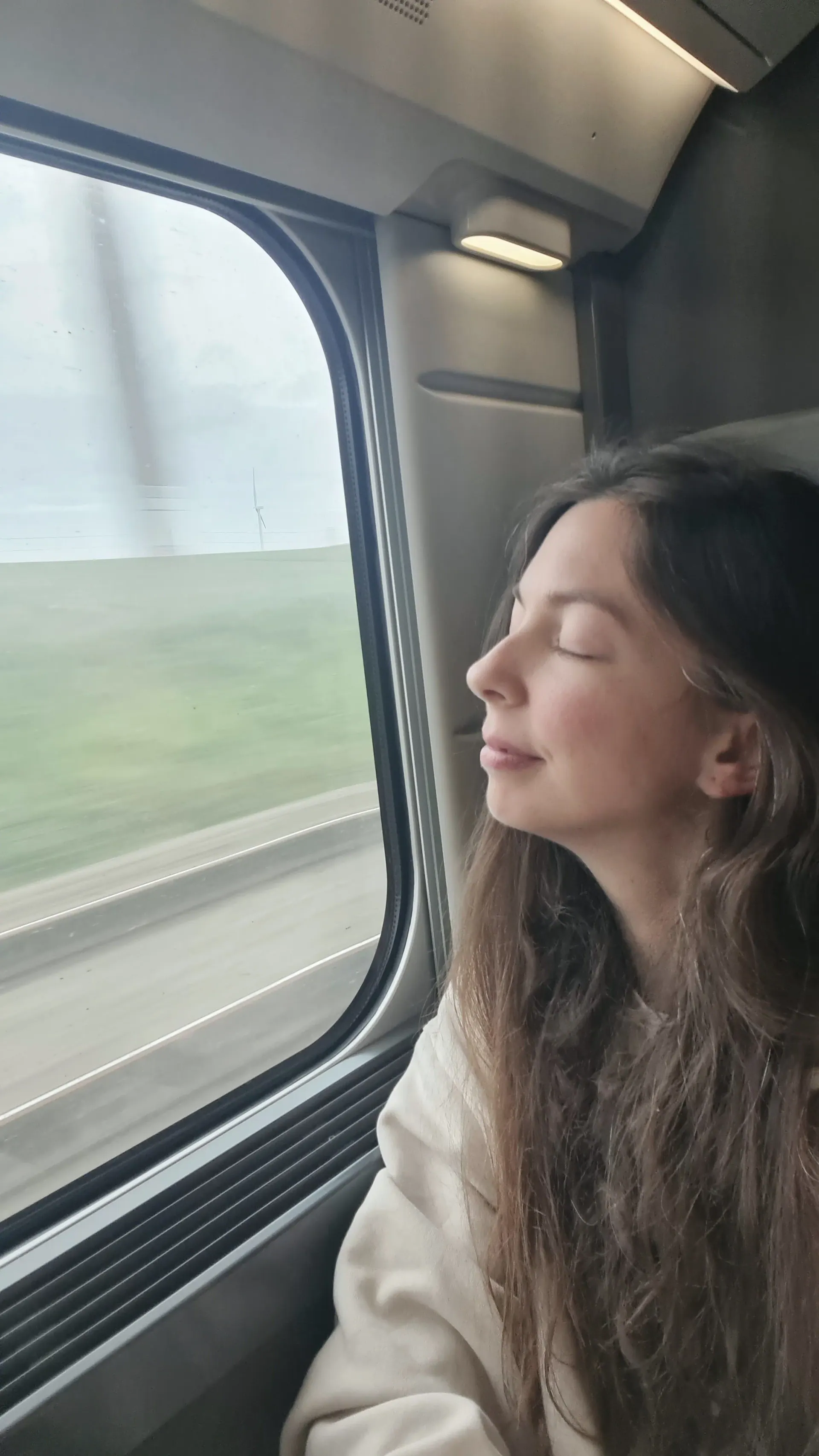 Ece leaning her head against a train window with her eyes closed