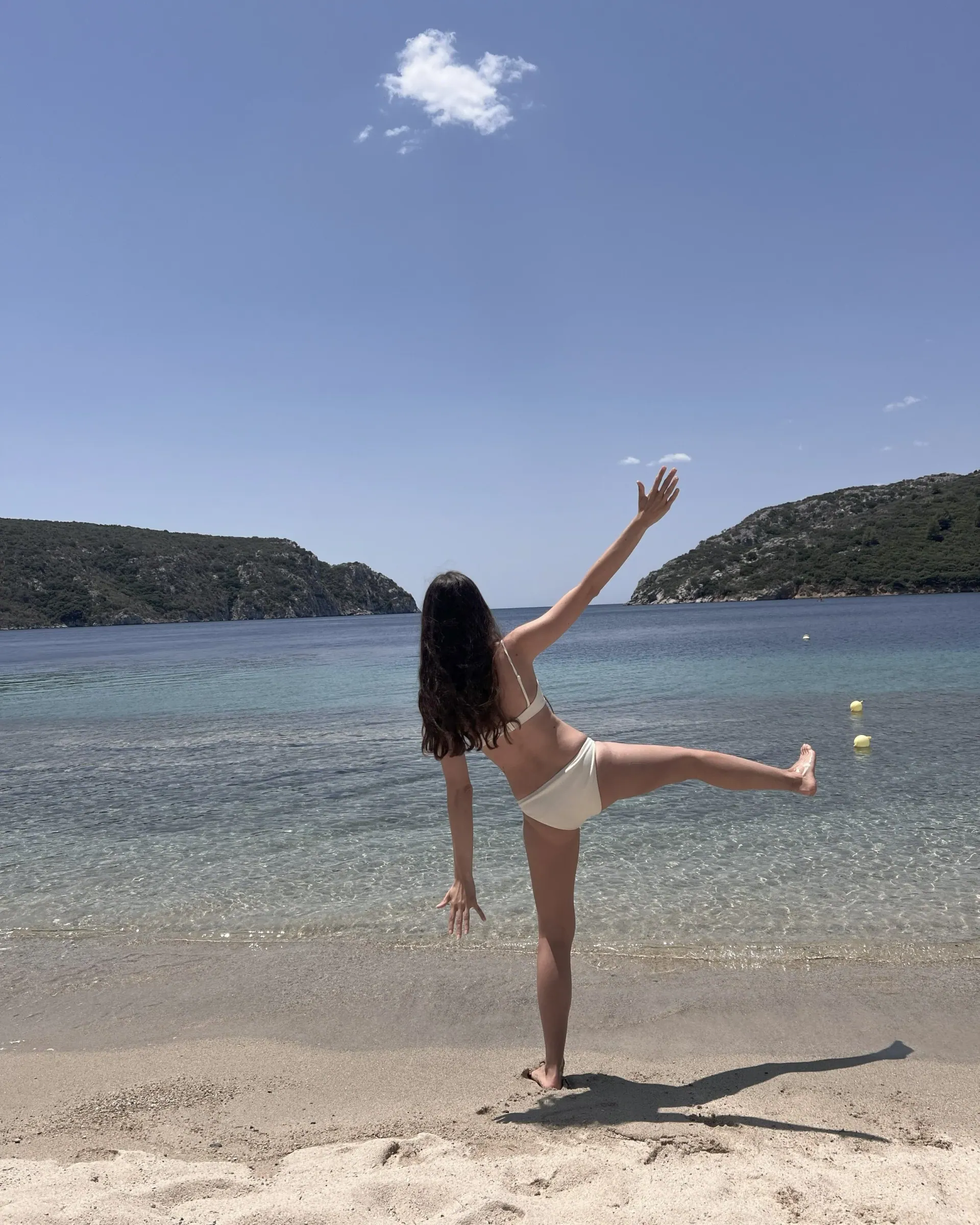 A woman balancing on one leg on the same beach, one arm reaching up and the other leg lifted out to the side