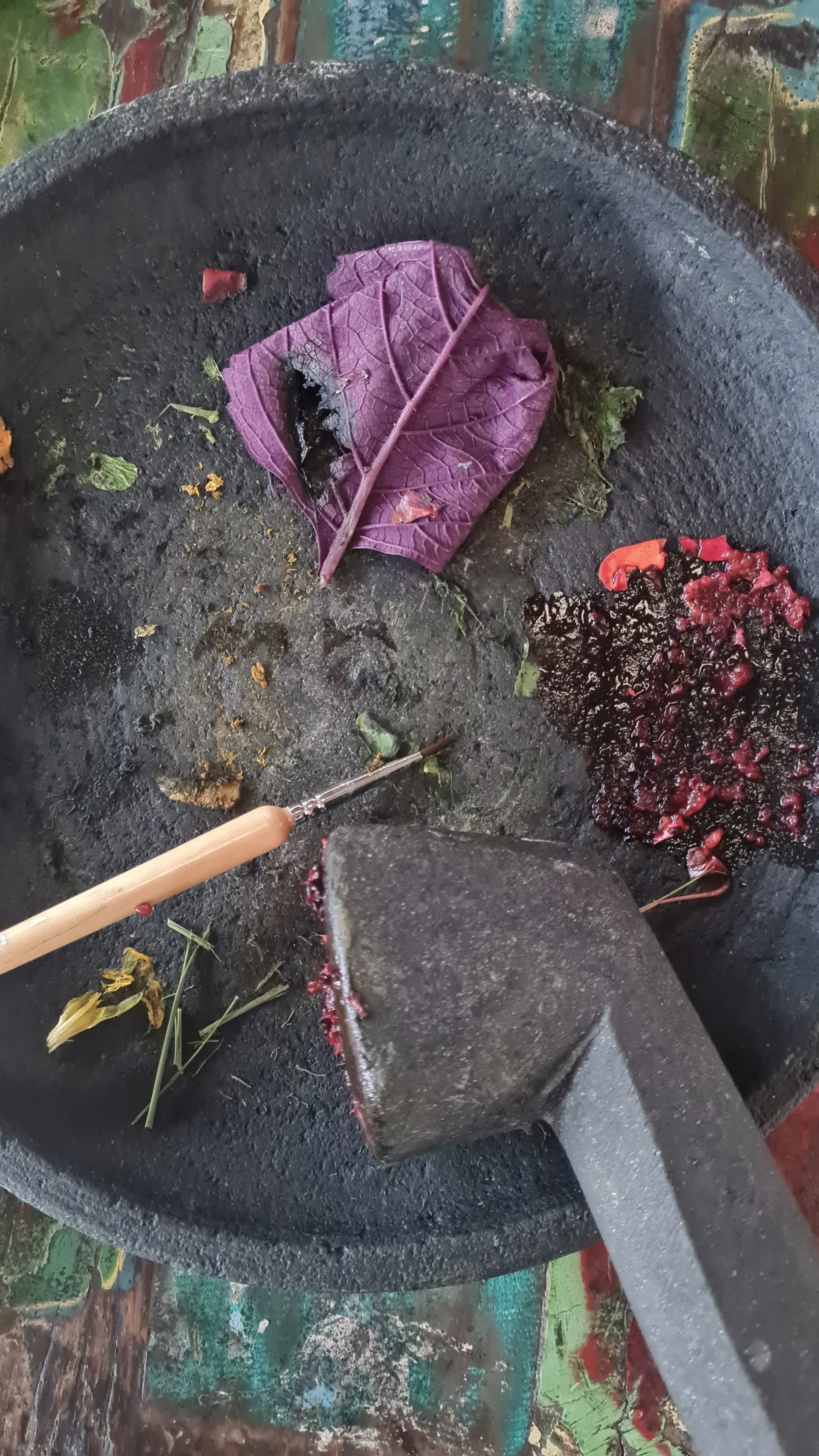 A stone mortar with crushed petals and leaves and a paintbrush