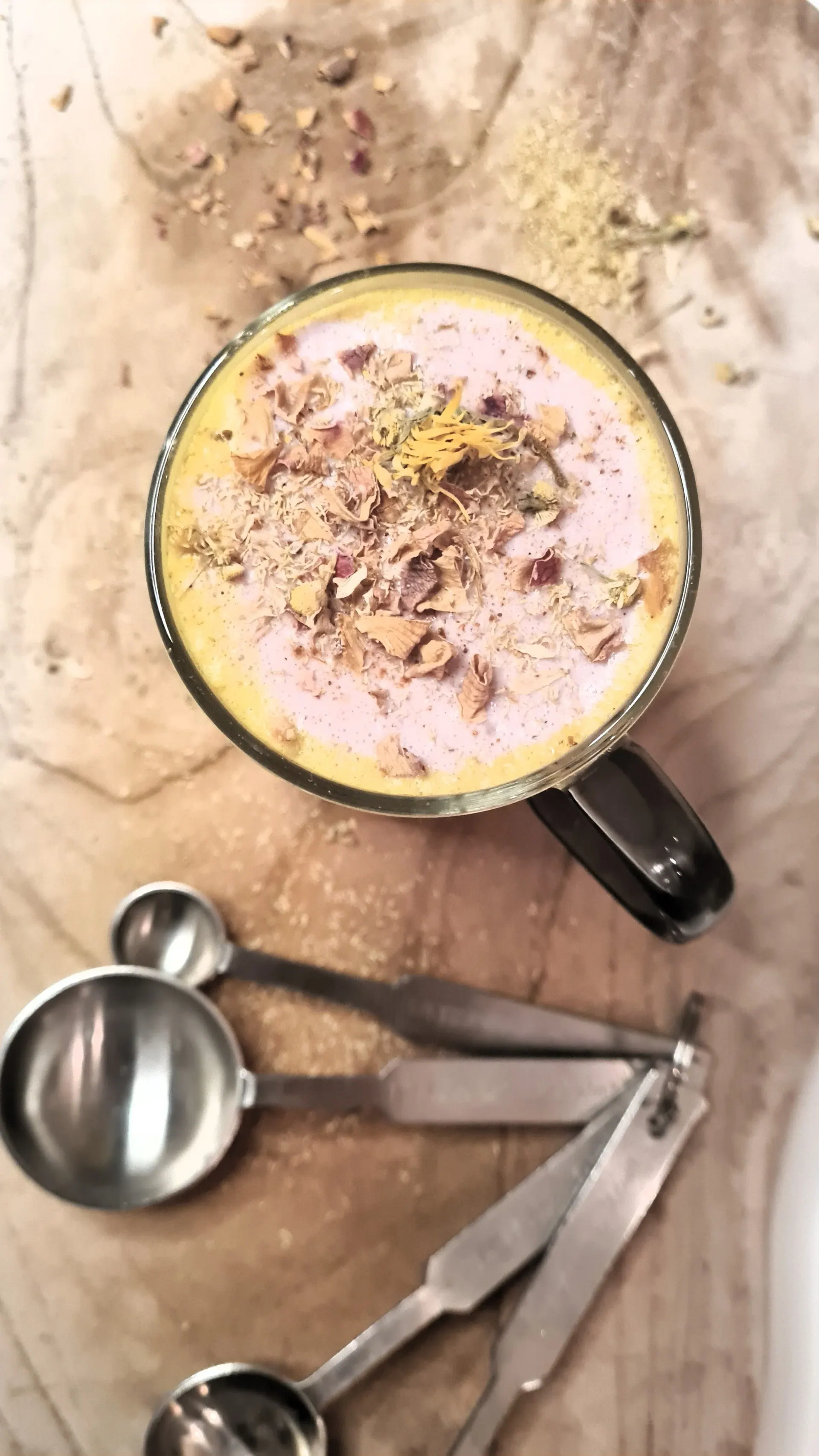 A mug of golden milk with rose petals next to measuring spoons