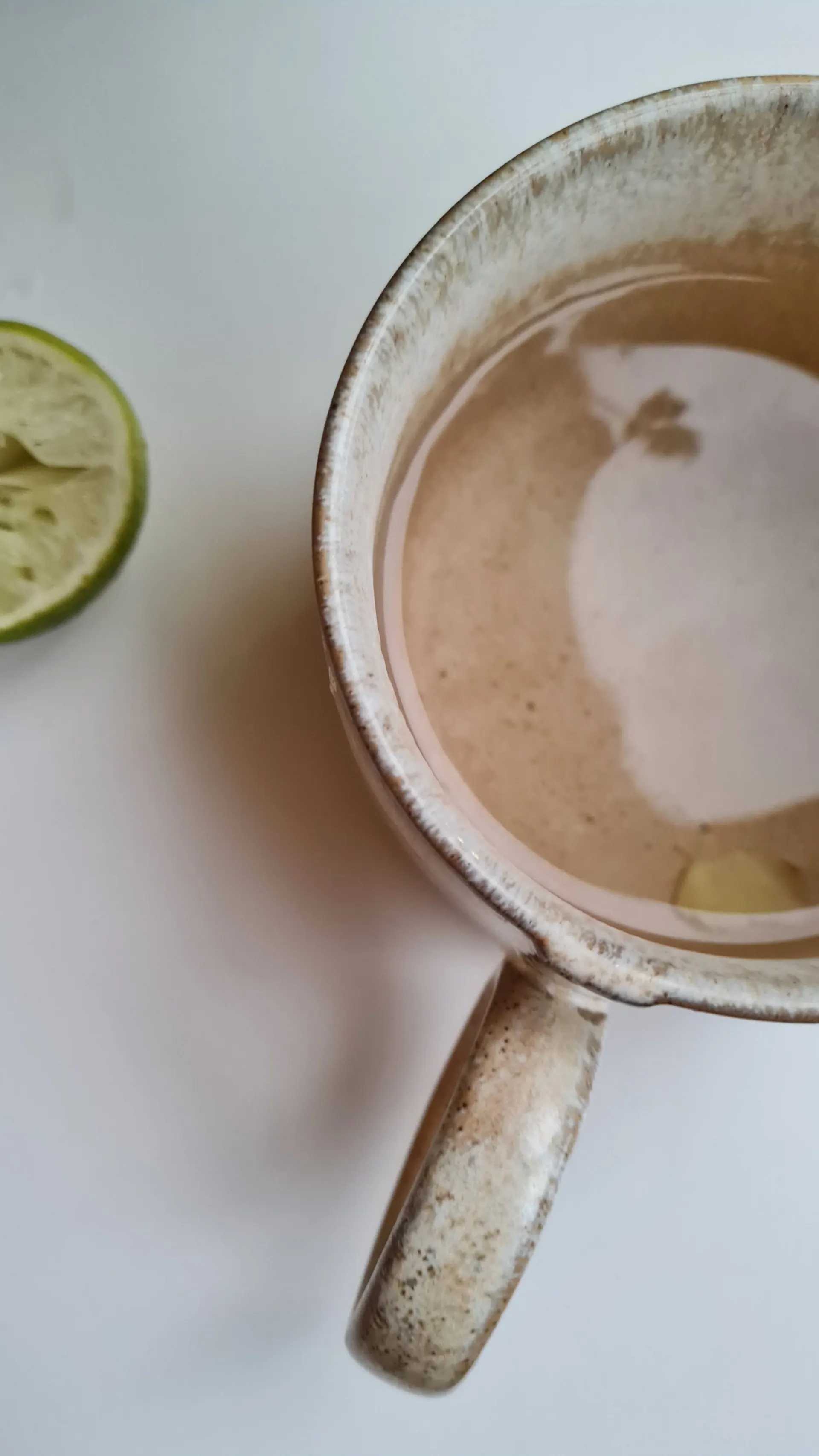 A drink in a speckled ceramic mug beside a squeezed half lime, seen from above
