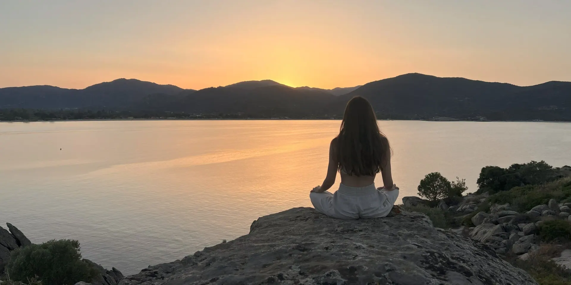 Ece meditating on a rock by the water at sunset